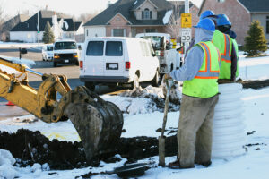 Excavator digging with two workers standing nearby